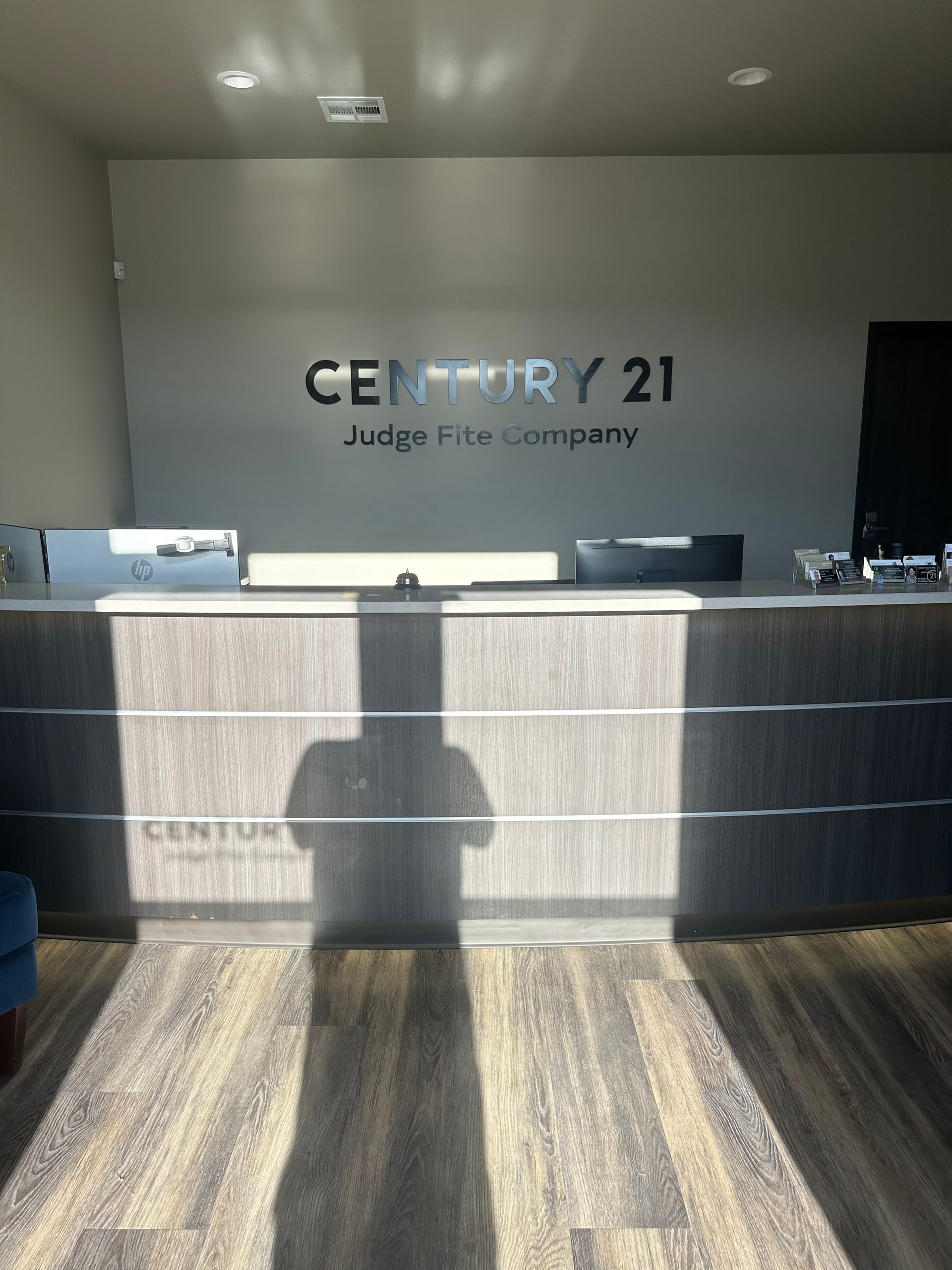 Empty Century 21 real estate reception desk with logo on the back wall and sunlight casting shadows on the floor