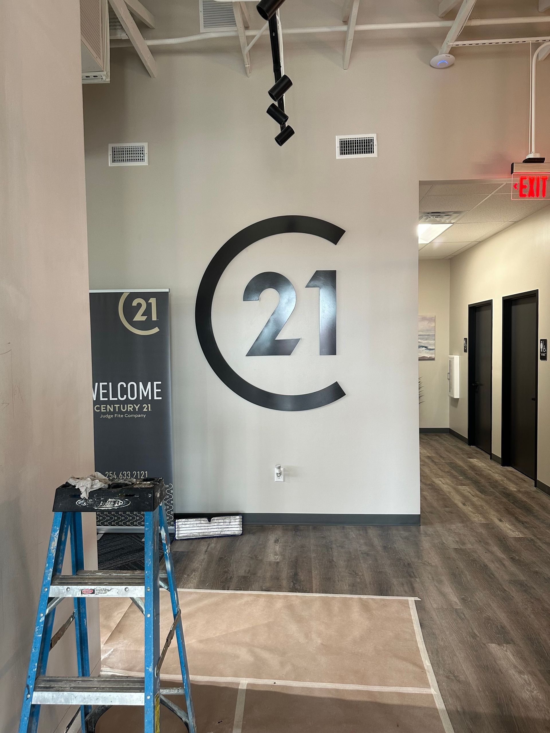 Interior hallway with large “21” wall logo, ladder, and construction materials on the floor