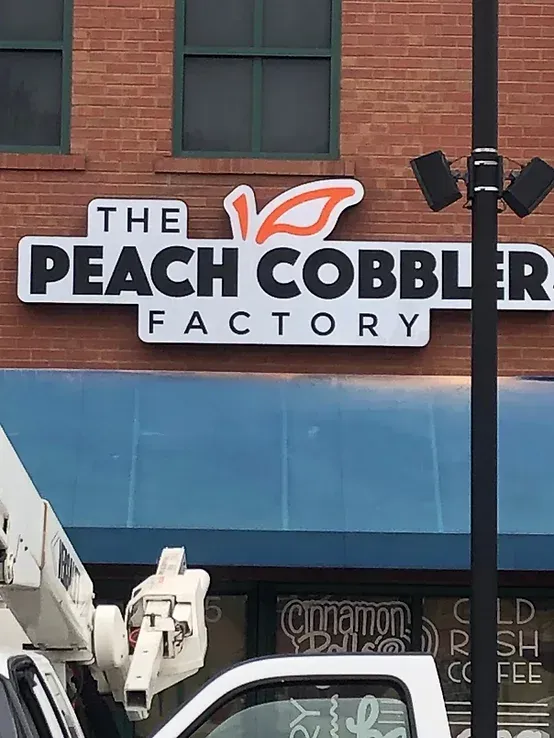 The Peach Cobbler Factory sign on a brick storefront with a blue awning