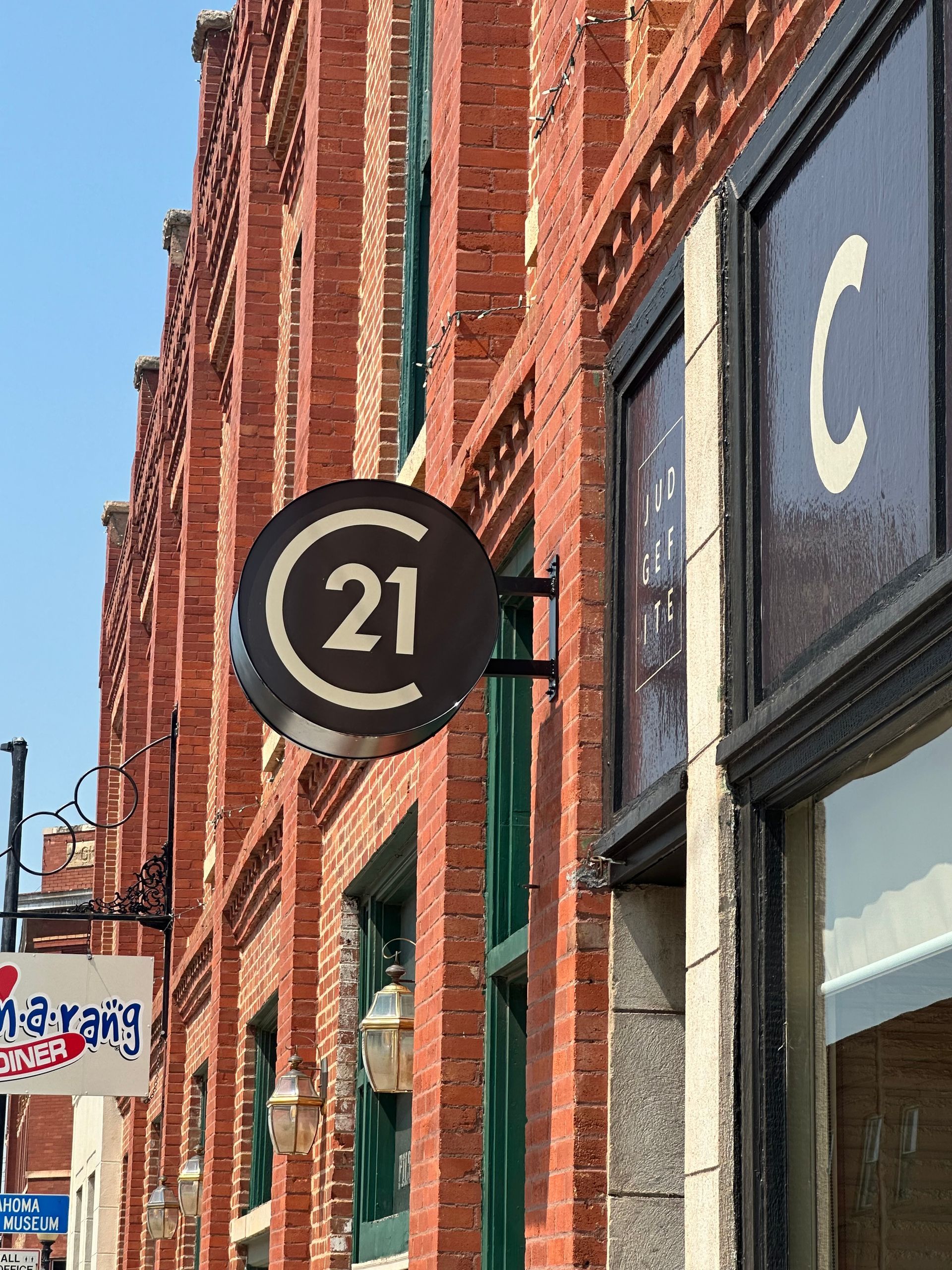 Street view of a brick building with a round black “21” sign and a store window marked “C”