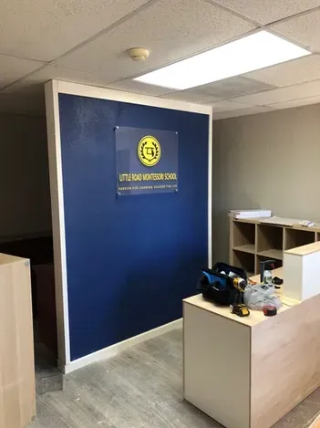 Office reception area with blue accent wall, front desk, and shelving under fluorescent lights