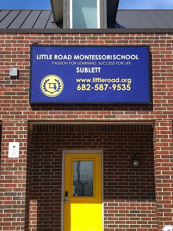 Brick building entrance with Little Road Montessori School sign and a bright yellow door