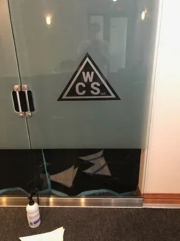 WC sign on a glass door above a small sanitizer bottle in a hallway.