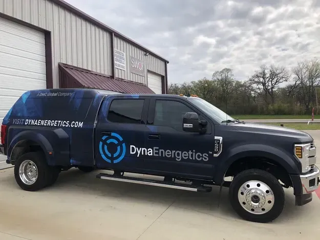 Blue DynaEnergetics service van parked outside a warehouse on an overcast day