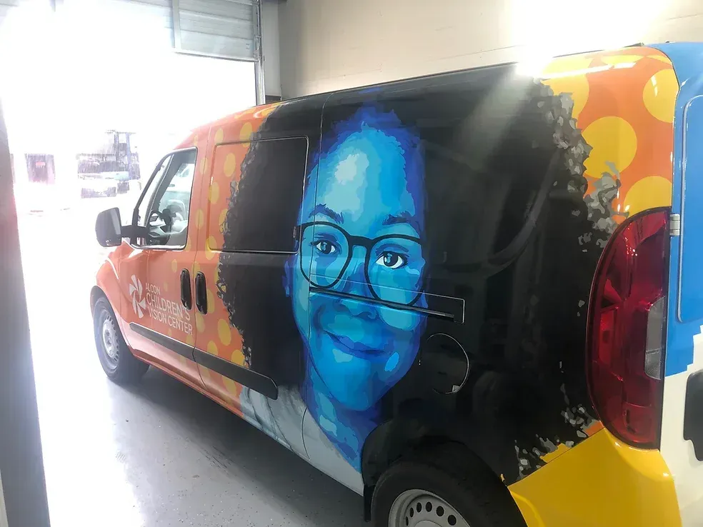 Colorful van wrap with a large smiling face portrait on the side, parked indoors.