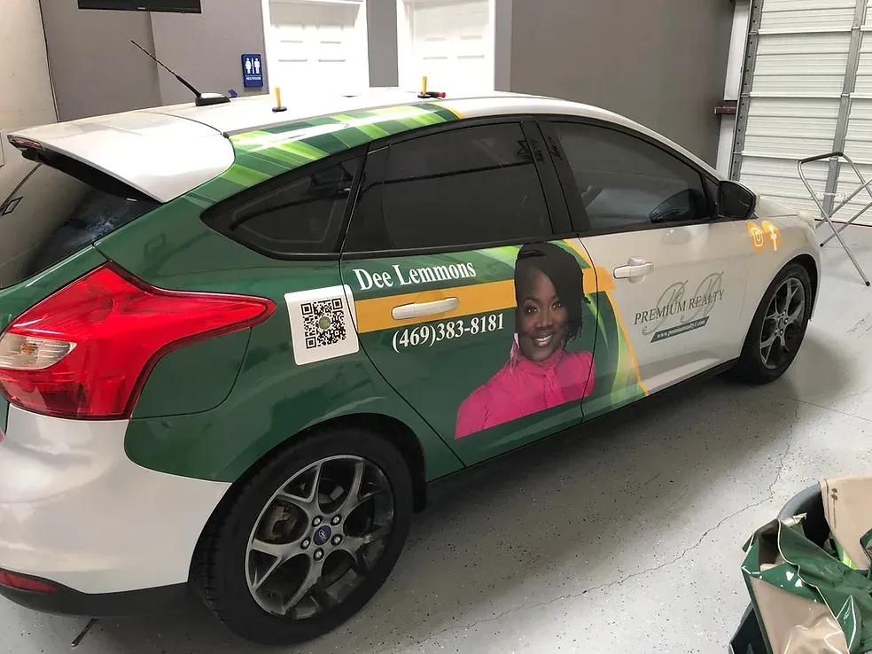 Wrapped silver sedan with green side panel and portrait ad parked in a garage