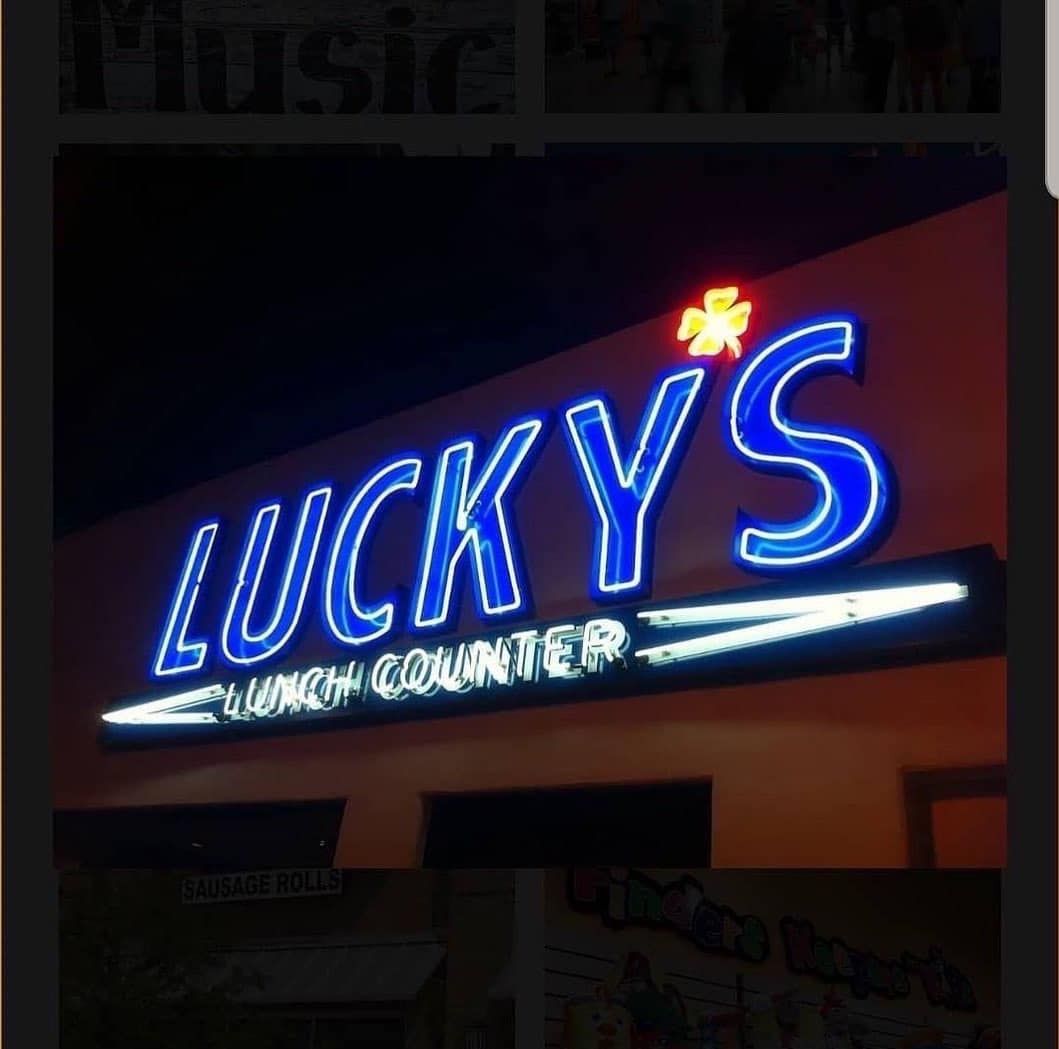 Neon sign reading “LUCKY’S” with a red flower and smaller “SUSHI COUNTRY” text on a dark building.