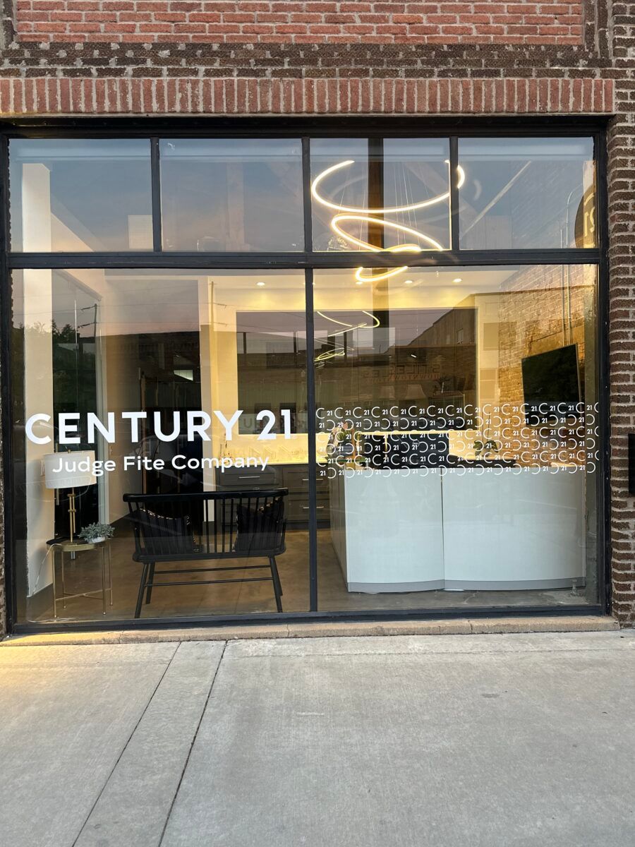 Storefront window of CENTURY 21 Joppe Fine Homes with modern interior lighting and chairs inside