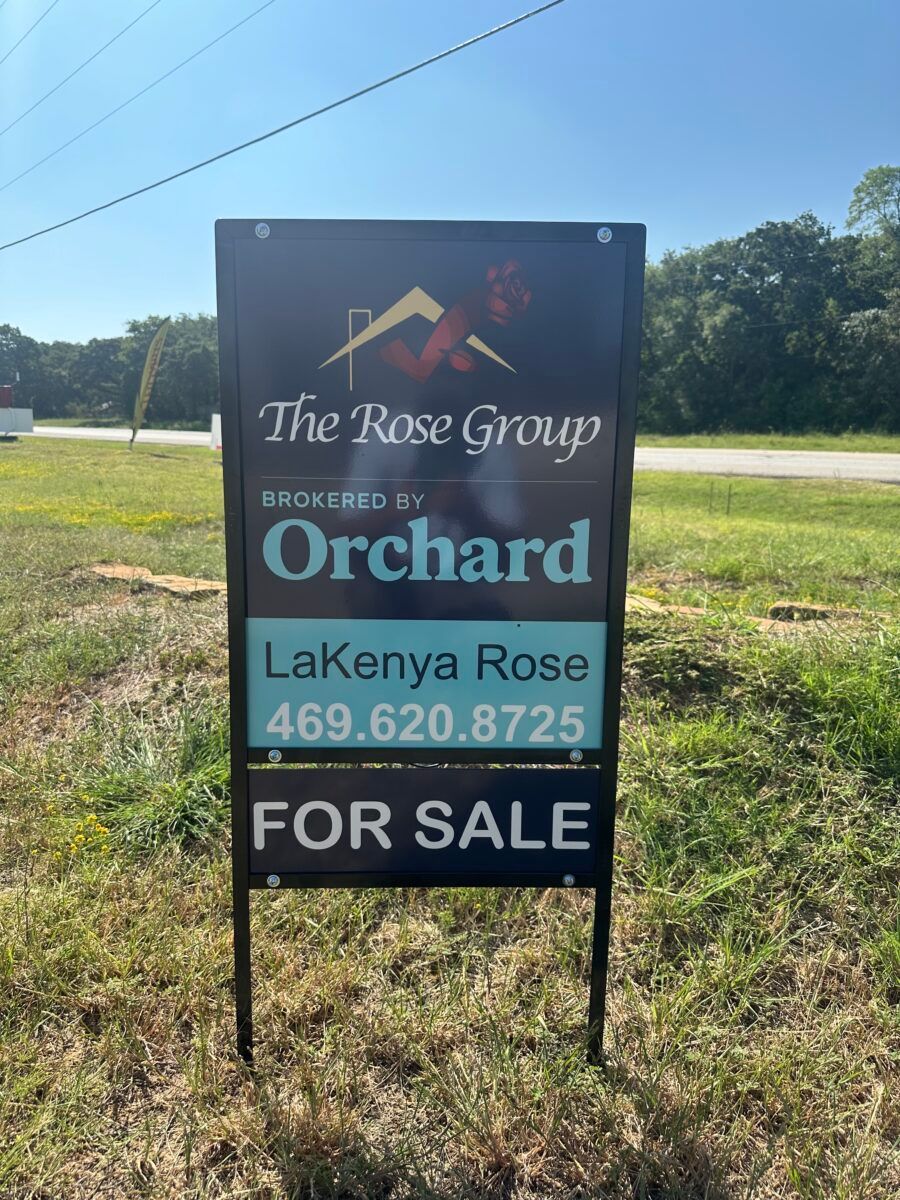 For sale sign for The Rose Group at Orchard, with LaKenya Rose and phone number, in a grassy field.