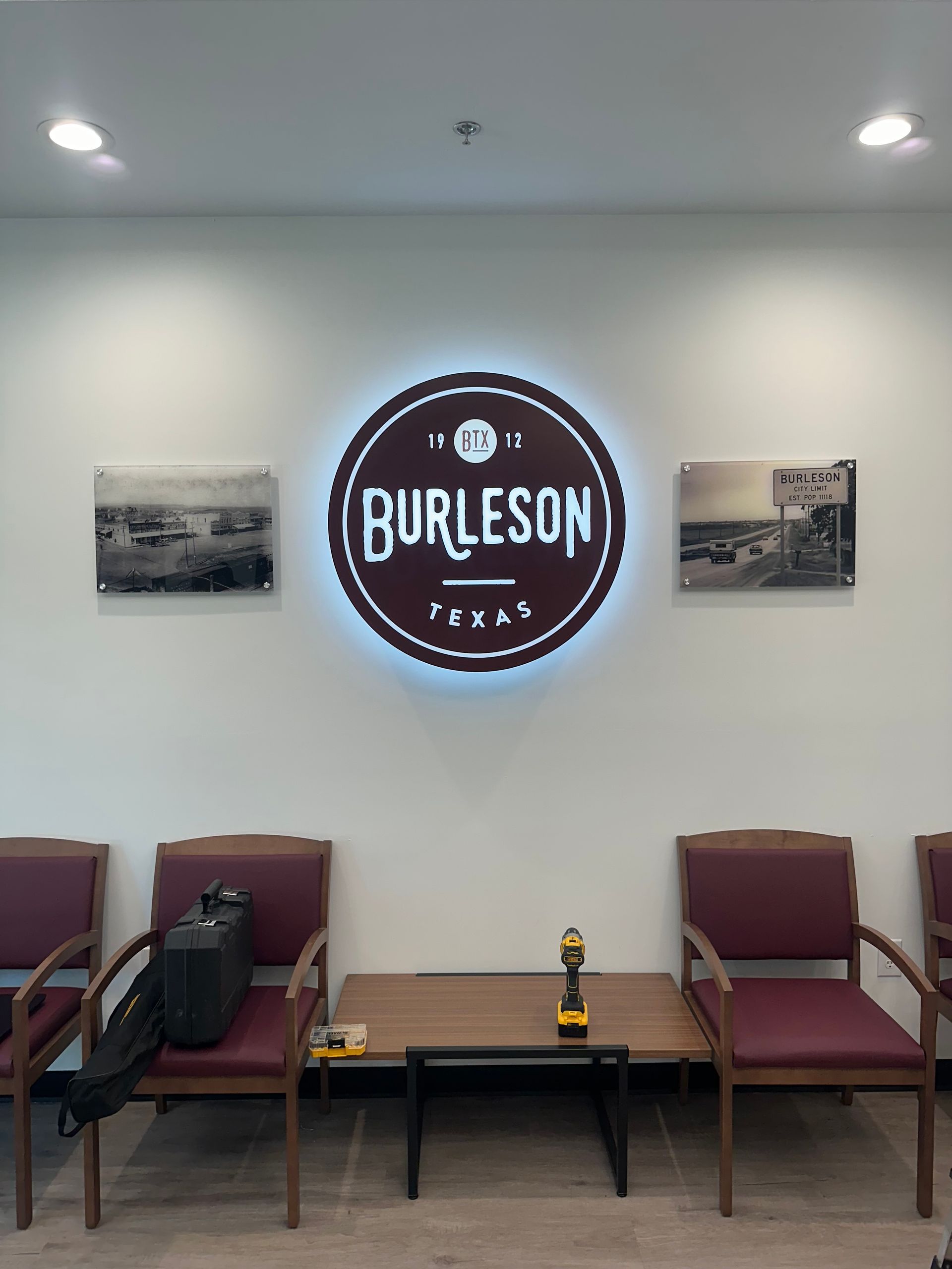Waiting area with chairs, tables, and a glowing Burleson sign on a wall