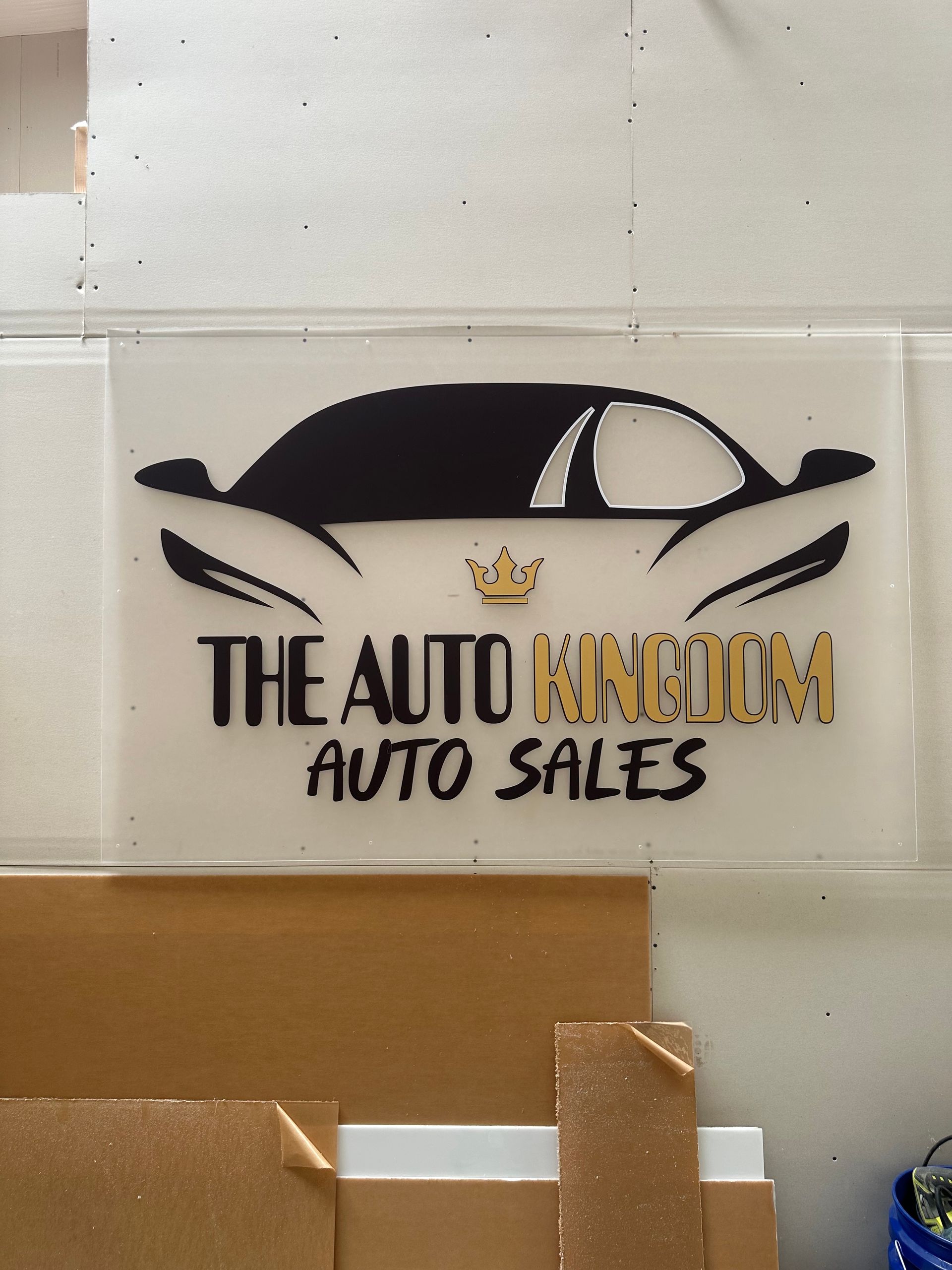 Logo for The Auto Kingdom Auto Sales with black car silhouette and crown on a wall sign