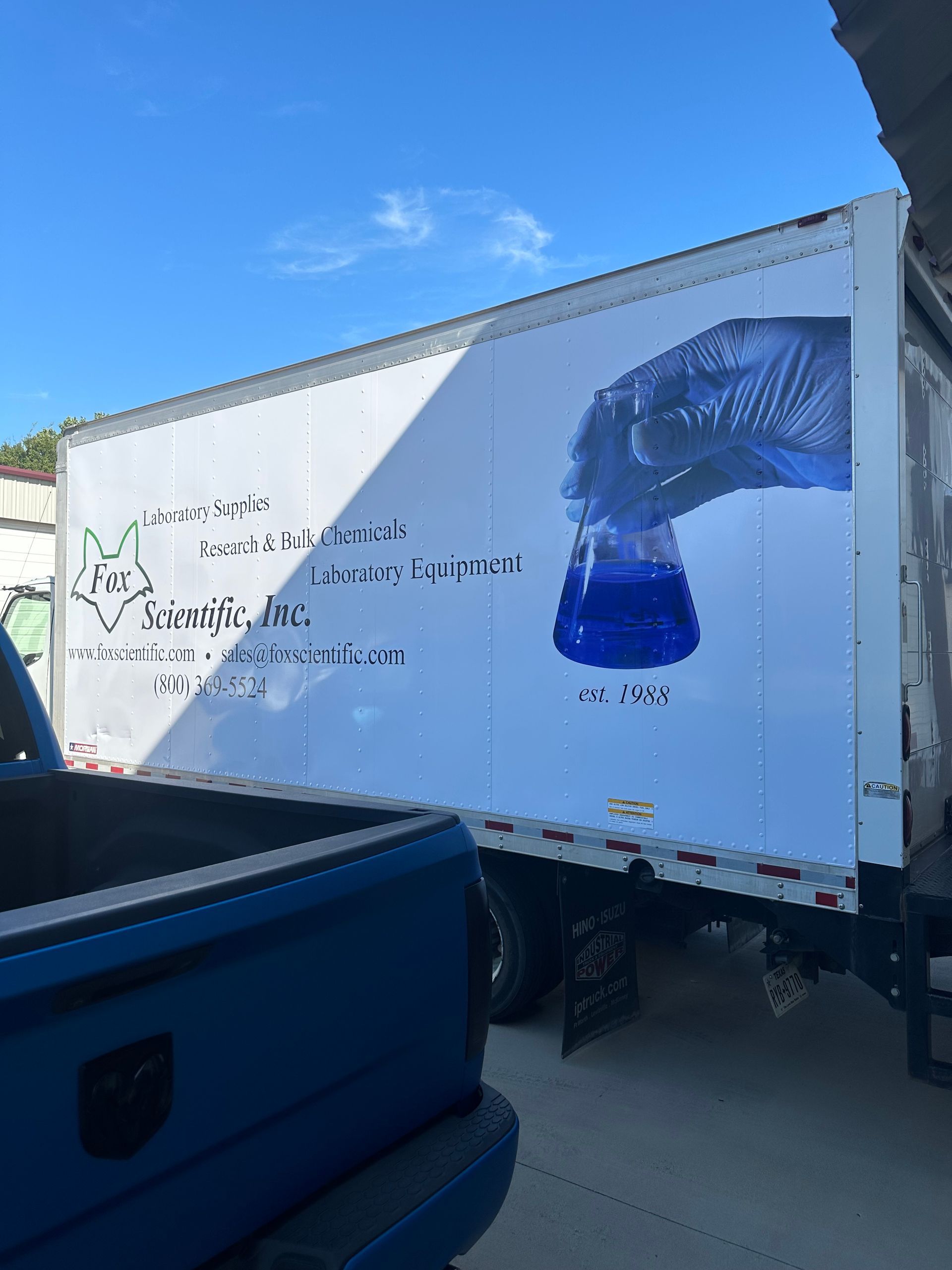 White semi-trailer with blue graphics parked beside a blue truck under a clear sky.