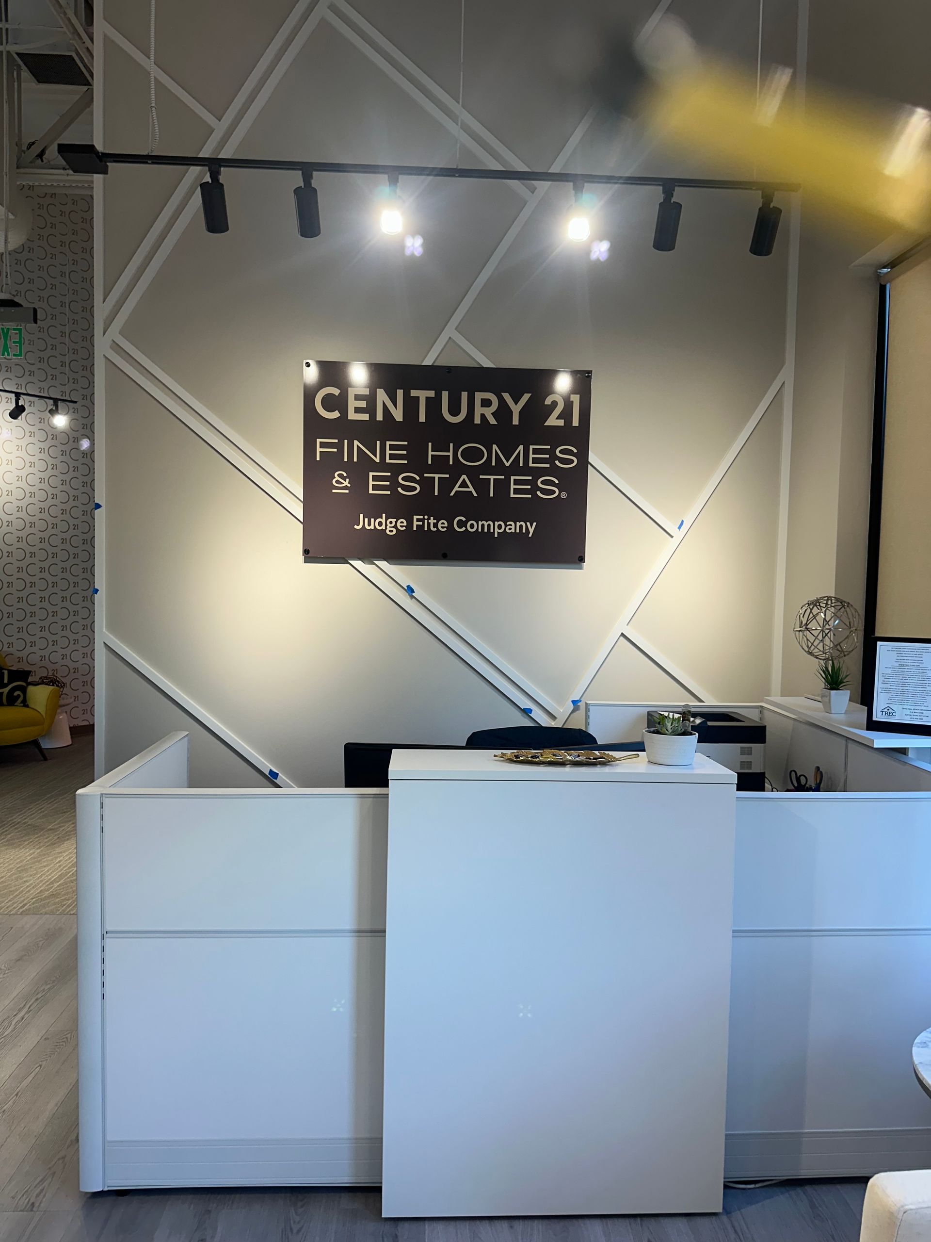 Century 21 real estate reception desk with white counters and illuminated logo wall