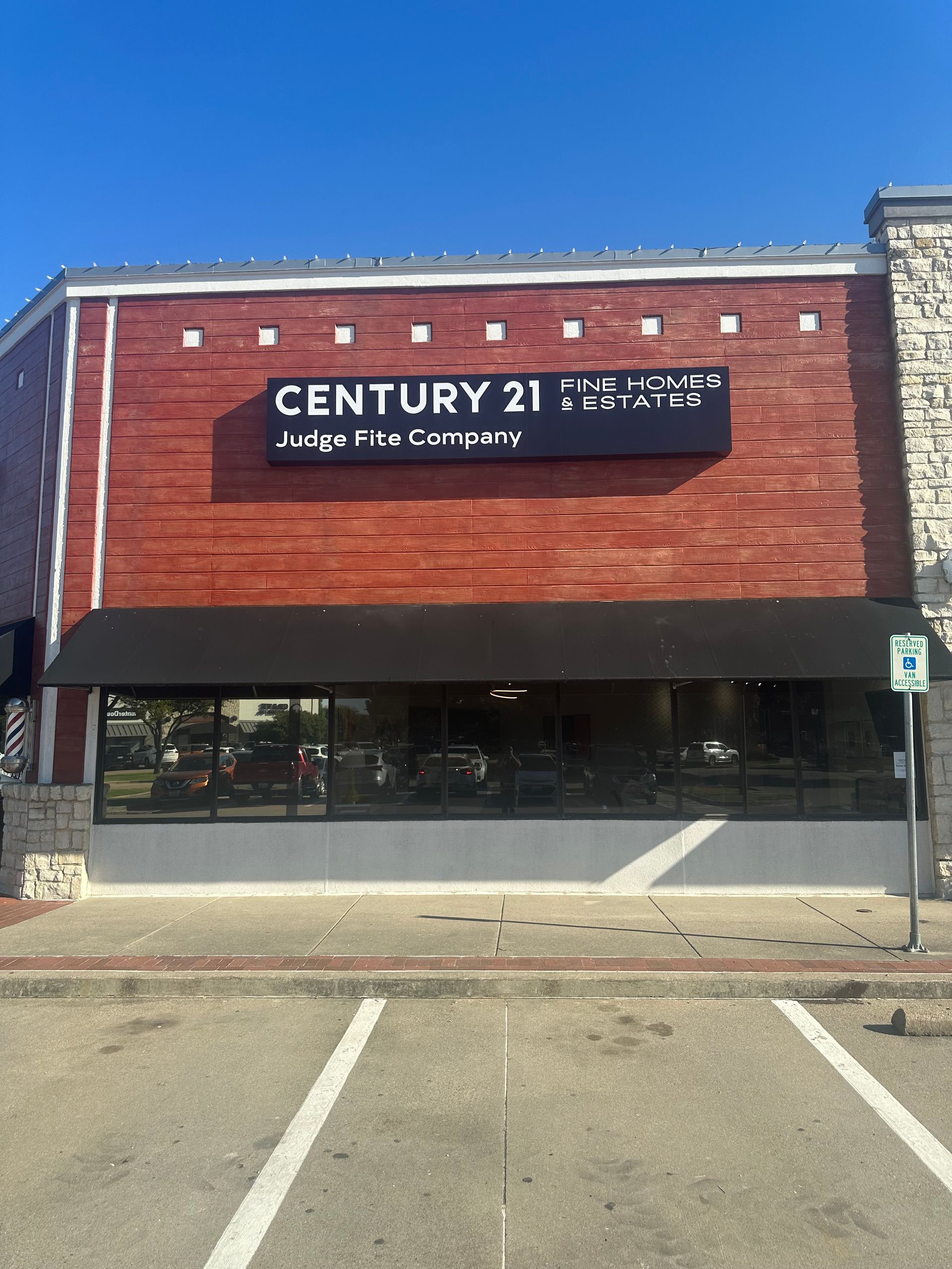 Century 21 storefront with red brick facade, black awning, and parking spaces in front