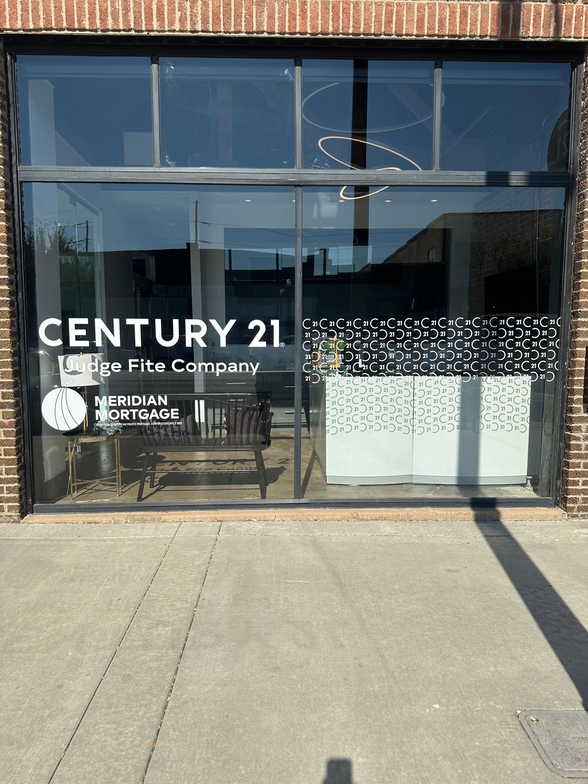 Century 21 real estate office storefront with glass windows and white signage on a brick building.