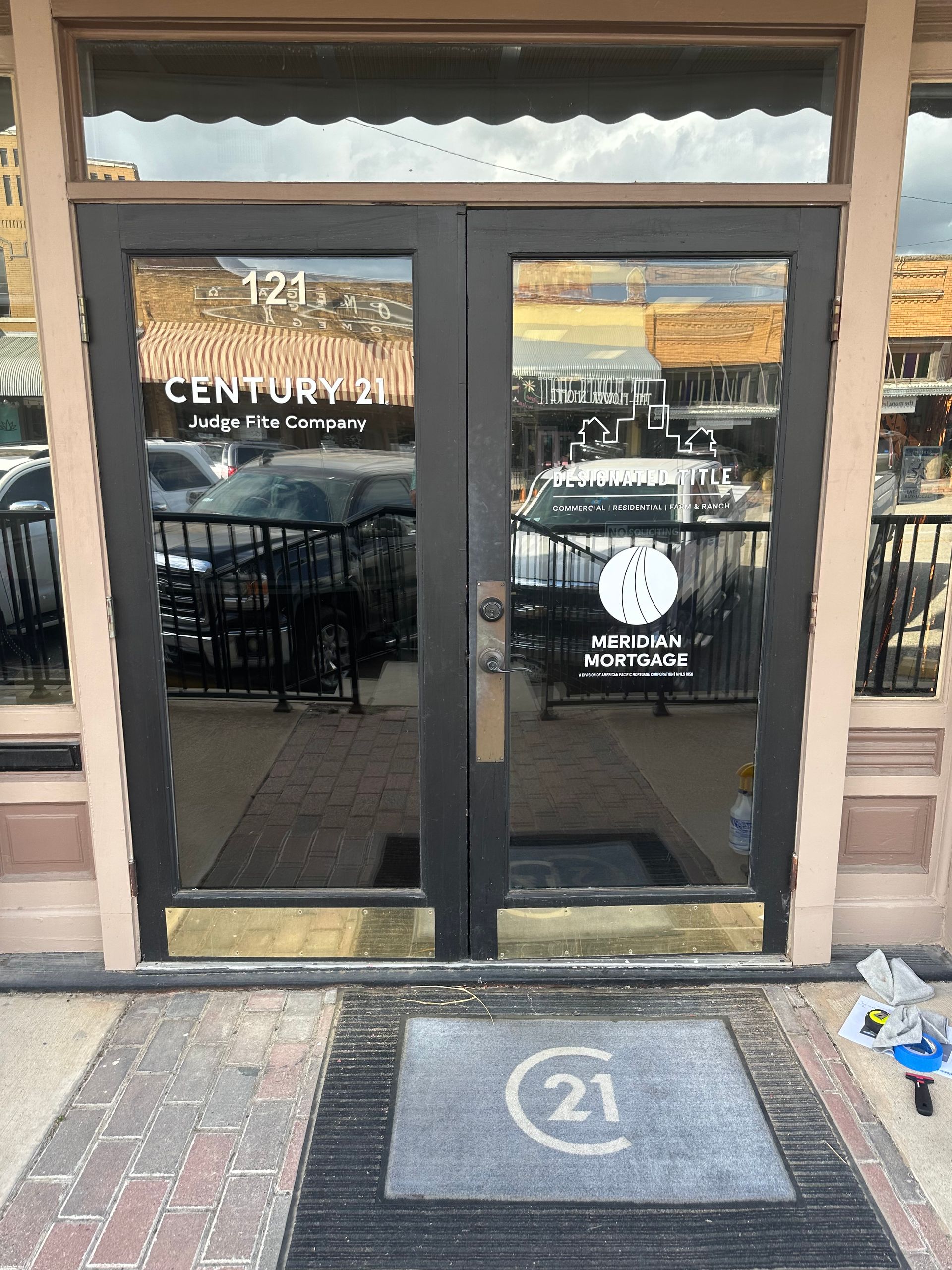 Glass double doors with a “21” doormat at a storefront entrance
