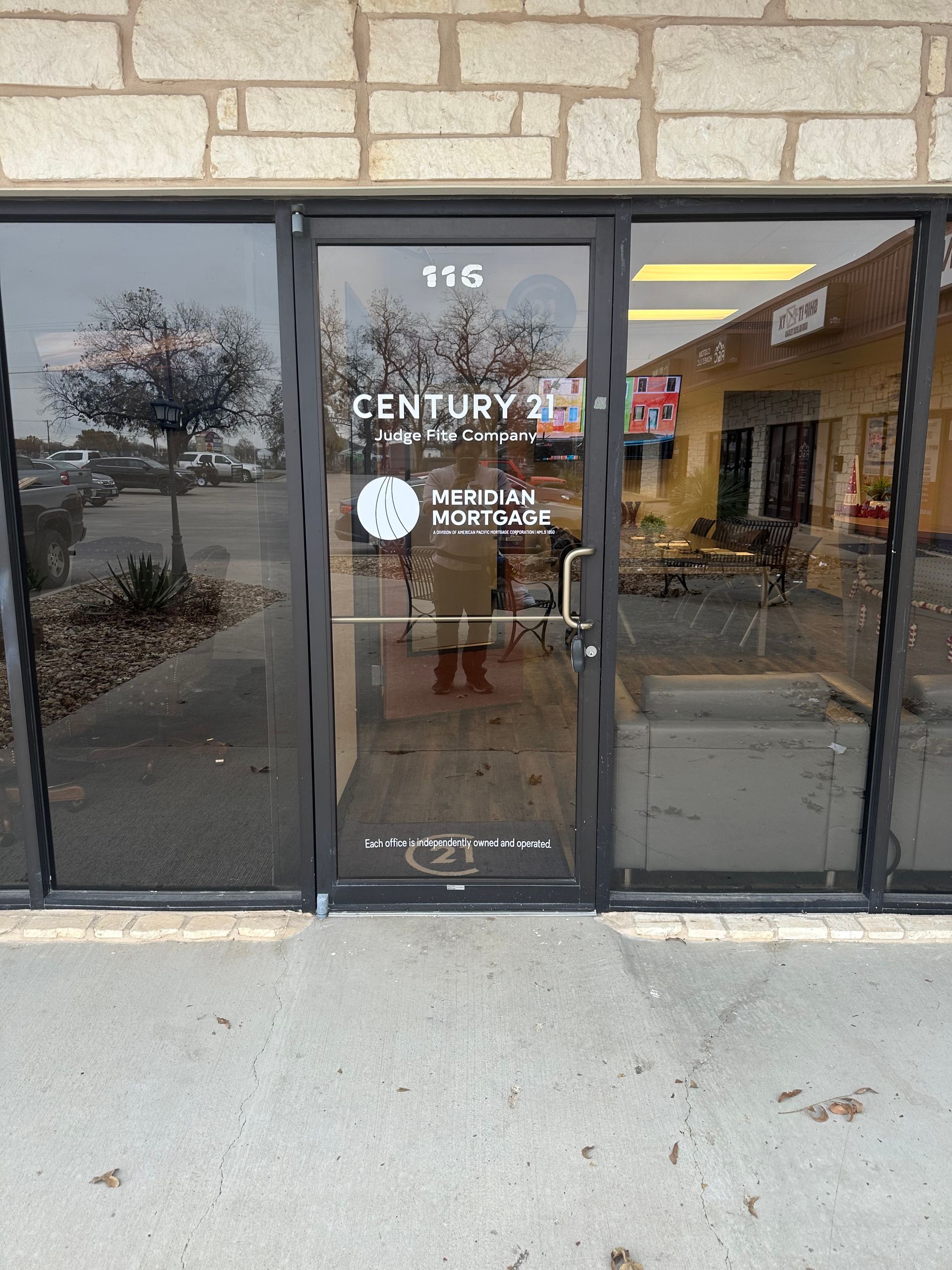 Storefront entrance with glass doors and windows, showing a CENTURY 21 office and “Now Open” sign.