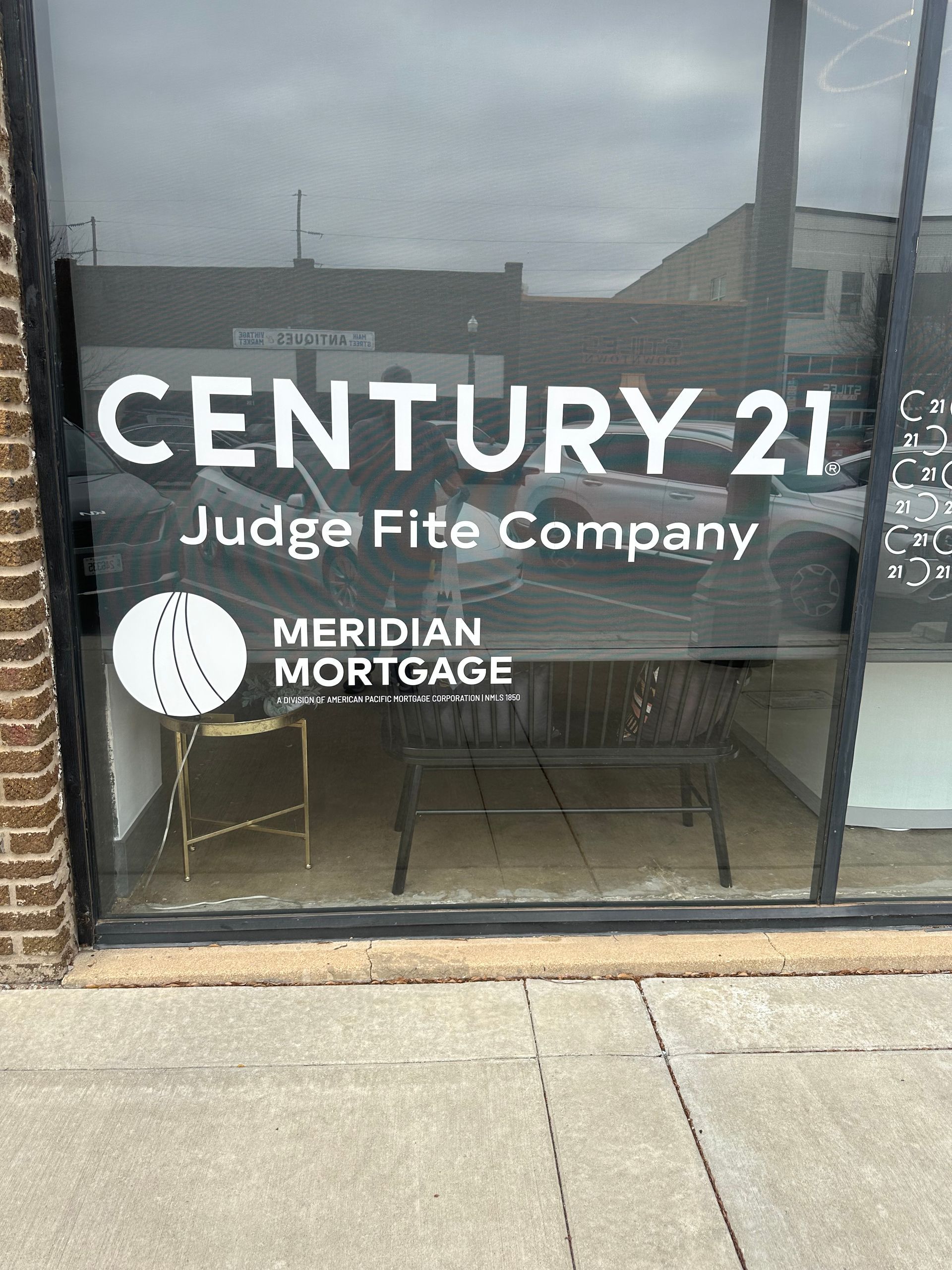 Storefront window with Century 21, Judge Fite Company, and Meridian Mortgage signs on a sidewalk.