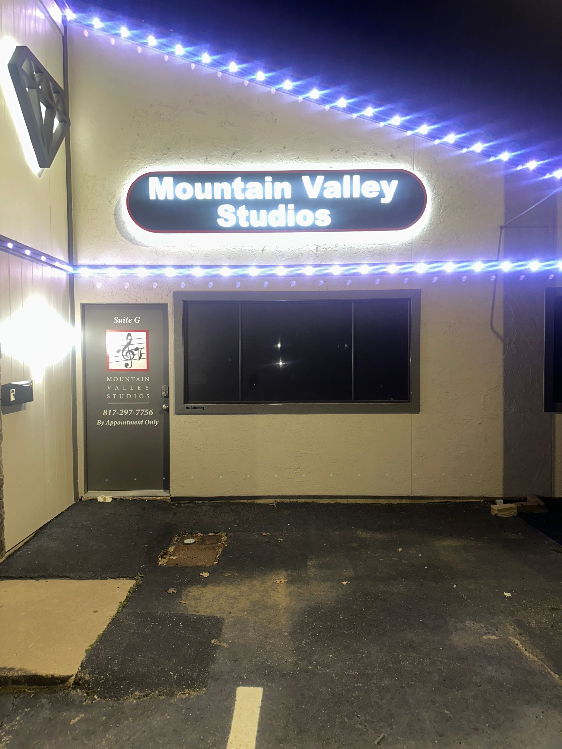 Mountain Valley Studios storefront at night, with glowing blue lights and a dark window.