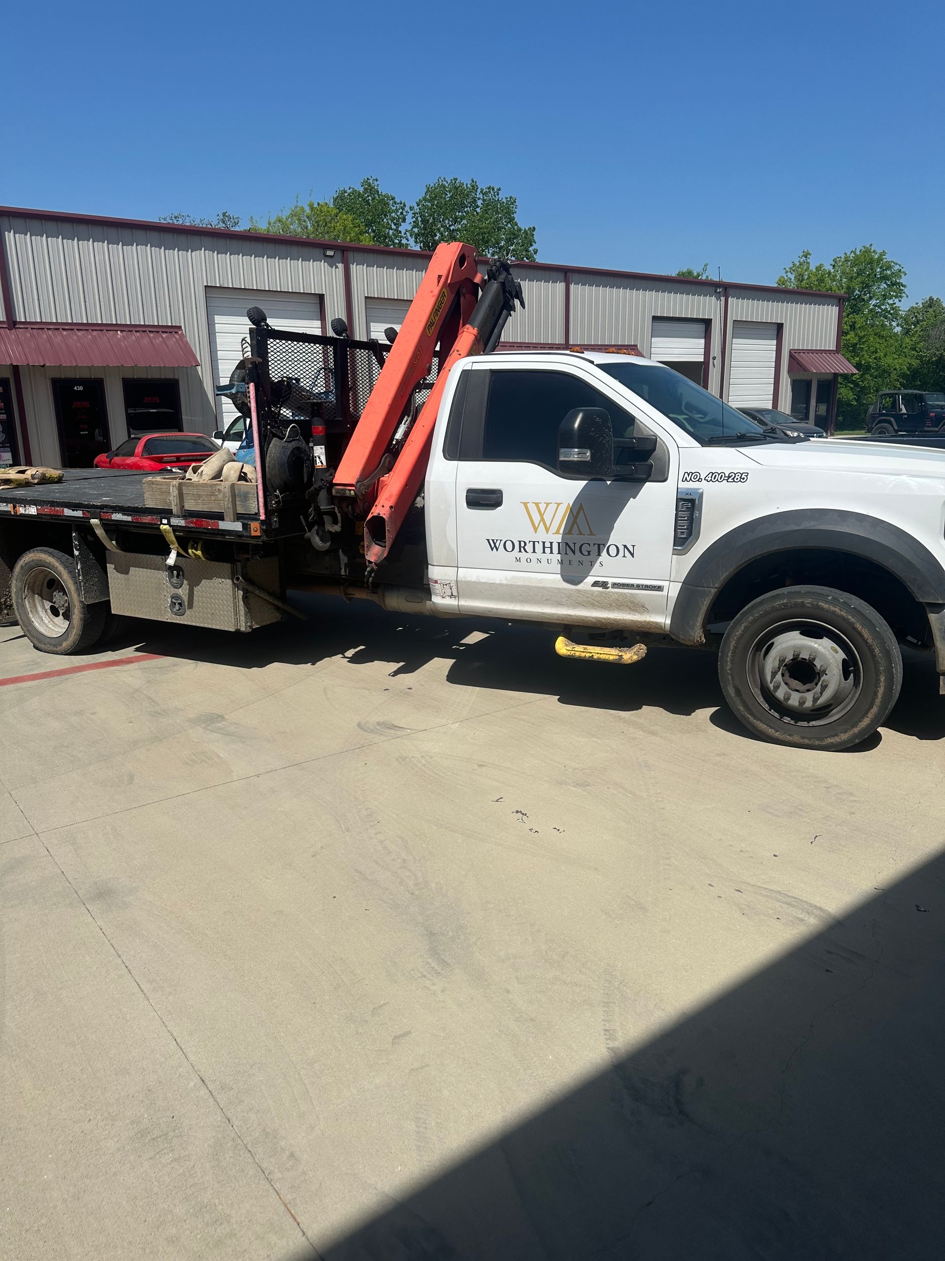 White utility tow truck with red crane parked on a dirt lot in front of a low building.