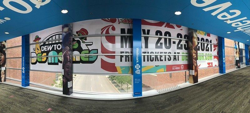 A banner advertisement at an outdoor event venue promoting Dew Tour Des Moines, May 20-23, 2021, with free tickets available.