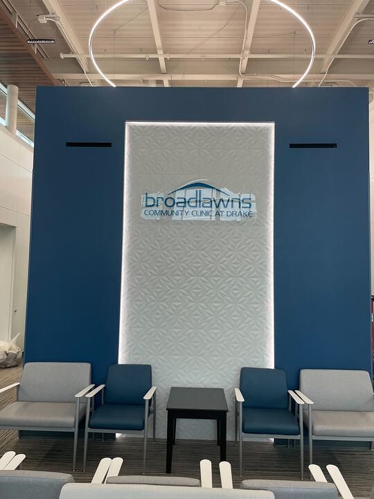 Waiting area with four chairs and a small table in front of a blue wall featuring the Broadlawns Community Clinic logo.