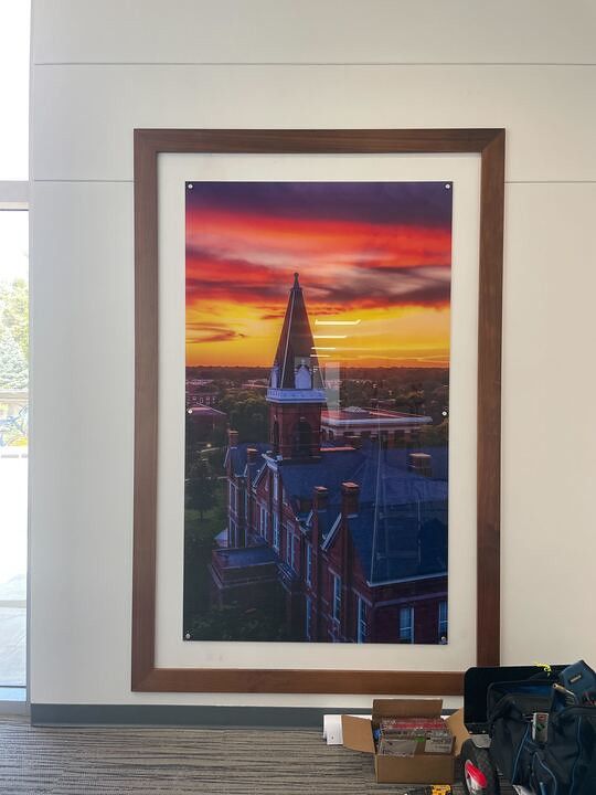 A large framed photo of Auburn University’s Samford Hall at sunset, set against a vibrant orange and purple sky.