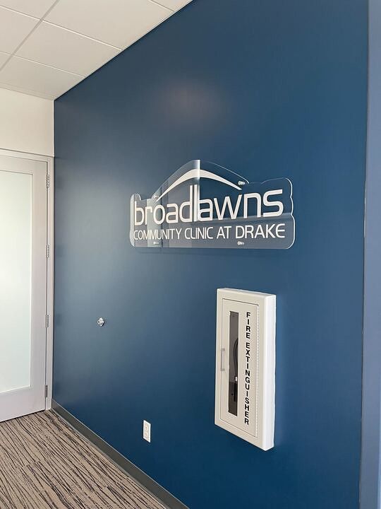 The Broadlawns Community Clinic at Drake sign on a blue wall with an adjacent fire extinguisher cabinet.