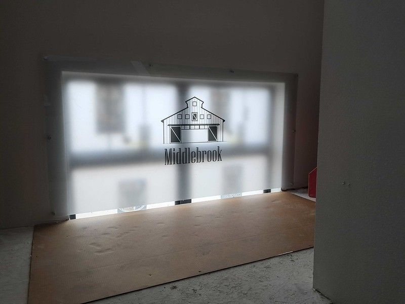 A frosted window with a Middlebrook barn logo, overlooking a light-filled area, in a room with a wood floor.