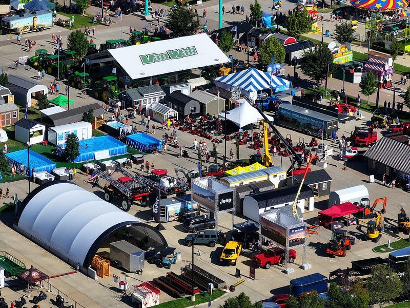 Aerial view of an outdoor trade show featuring tents, agricultural machinery, and displays in a paved lot.