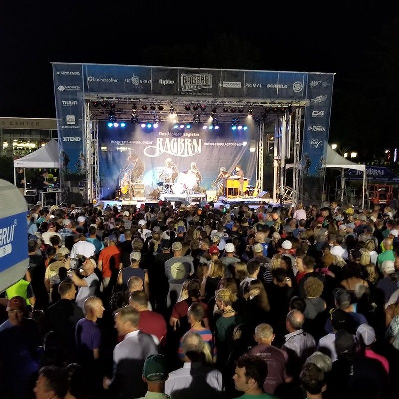 A nighttime outdoor concert with a large crowd facing a brightly lit stage with a musical group performing.