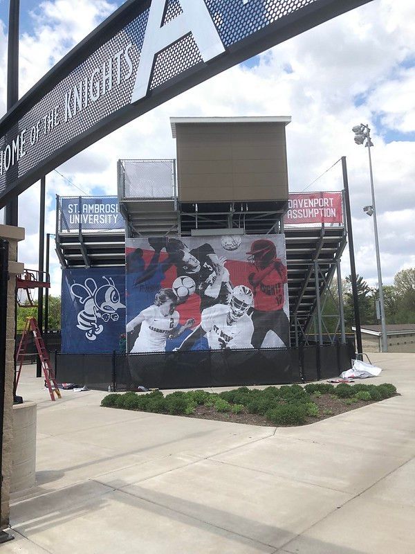Bleachers with a large banner of sports action, a school mascot, and St. Francis University branding at a stadium entrance.