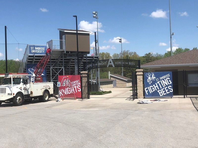 St. Ambrose University athletic stadium entrance with signs for the Fighting Bees and Knights, and a utility truck nearby.