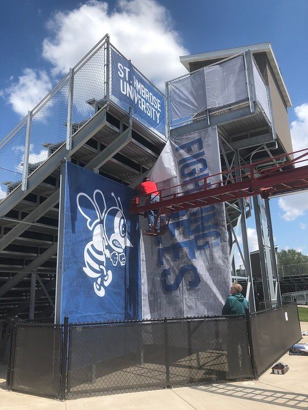 St. Ambrose University stadium bleachers featuring a large Fighting Bees mascot banner under a sunny, blue sky.