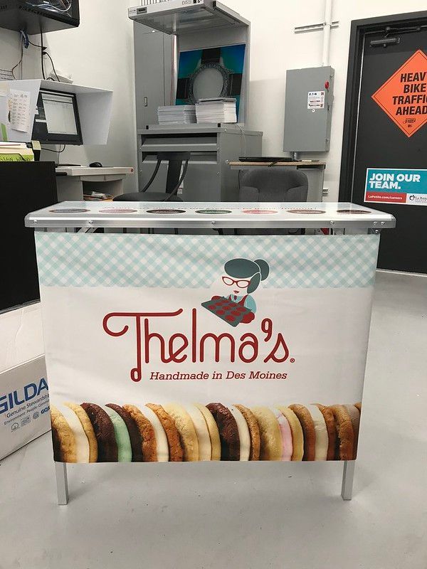 A Thelma's portable display stand featuring a branded sign with a cartoon mascot above a row of ice cream sandwiches.