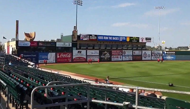 Empty stadium seats face a grassy baseball field with an outfield wall covered in various corporate advertisements.