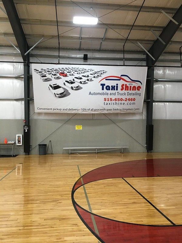 A banner for Taxi Shine detailing services hangs on the wall of an indoor basketball court.