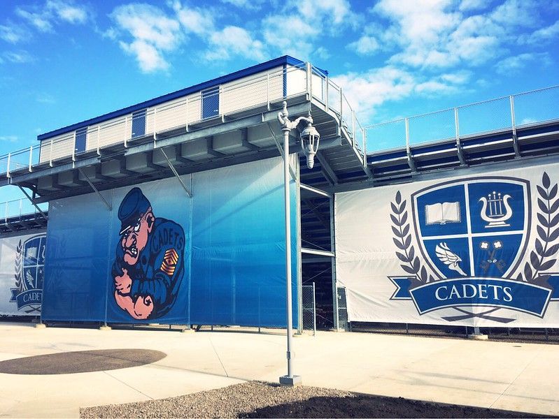 A mural of a blue-clad cadet mascot and a blue shield crest labeled CADETS on the side of a stadium under a blue sky.