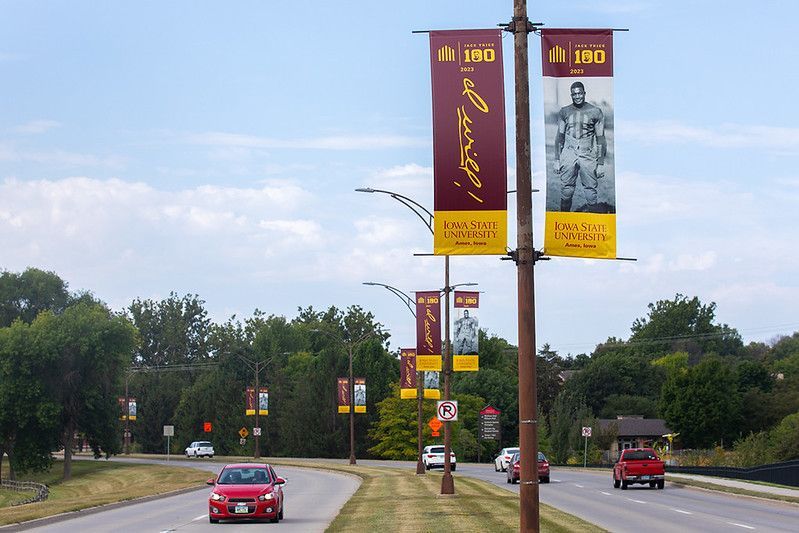 A street with light poles adorned with maroon and yellow commemorative banners, featuring cars driving on the road.