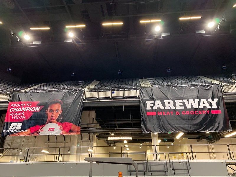 Two banners hang in a stadium: one featuring a person holding a ball, the other displaying the Fareway Meat & Grocery logo.