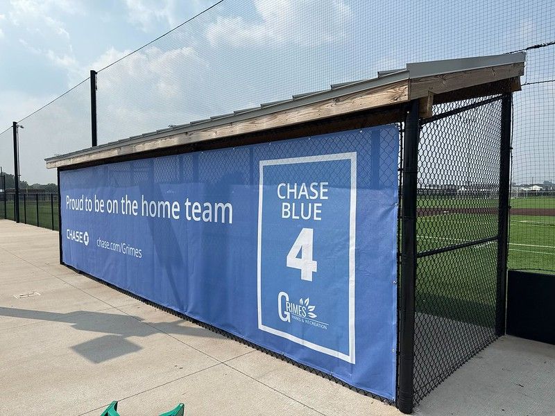 A blue banner on a baseball dugout fence reads 