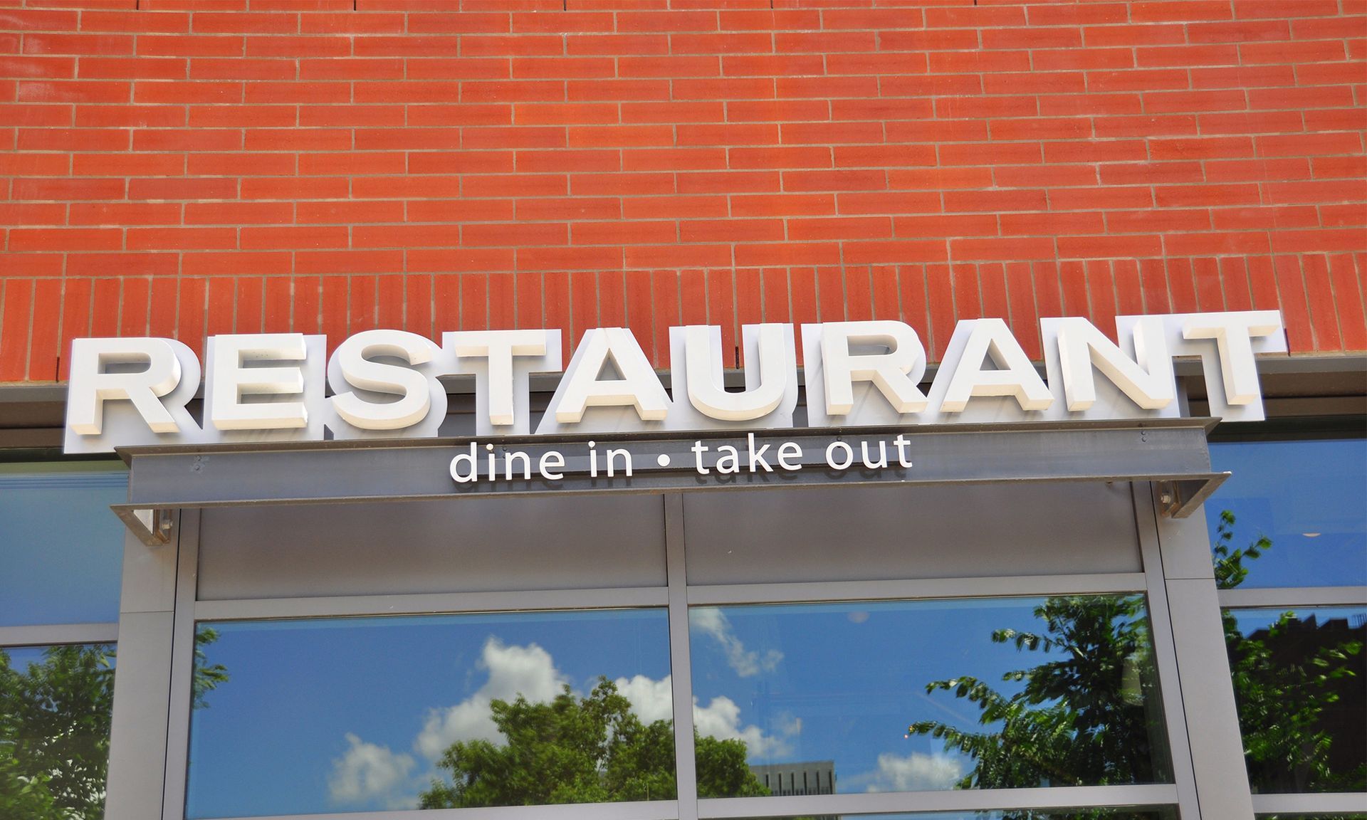 A brick building exterior featuring a white, 3D sign that reads "RESTAURANT" above the text "dine in • take out".