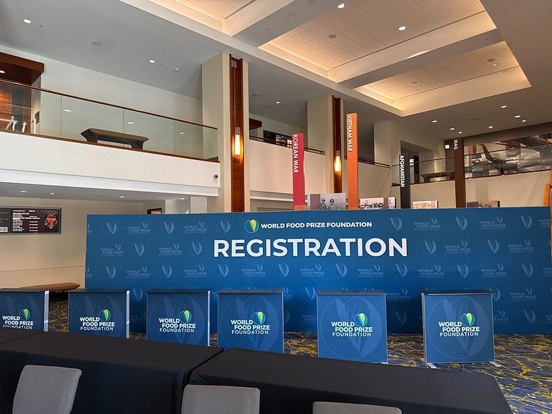 A registration area for the World Food Prize Foundation in a lobby with blue branding signage and black table covers.