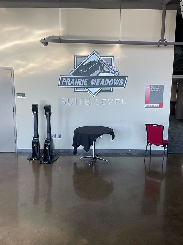 A hallway at Prairie Meadows Suite Level with two stanchions, a small round table with a black cloth, and a red chair.