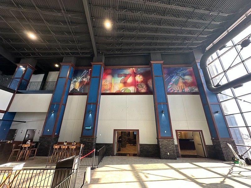A spacious, modern hall featuring three blue pillars and colorful wall art above two doorways with a high industrial ceiling.