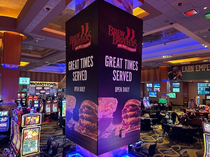 A large, square pillar in a dimly lit casino features Brew Brothers advertisements with burgers and 