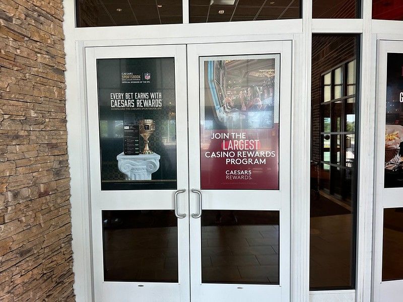 Glass double doors feature Caesars Rewards posters against a stone wall in an indoor setting.