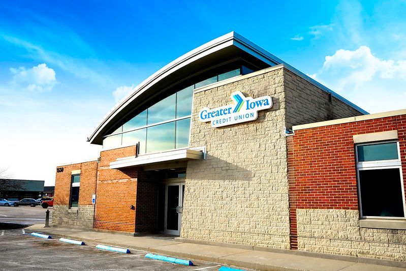 Greater Iowa Credit Union building with a tan stone facade, red brick accents, and a large curved roof against a blue sky.