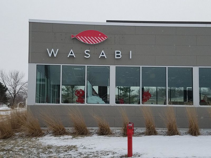 Exterior view of the Wasabi restaurant with a red fish logo and white text on a grey wall, set against a snowy landscape.