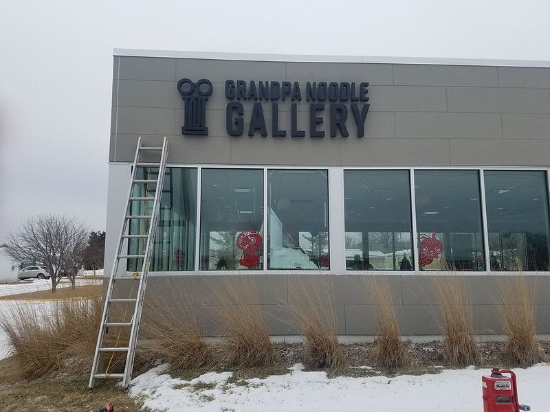 A metal ladder leans against the exterior wall of a commercial building with signage reading 